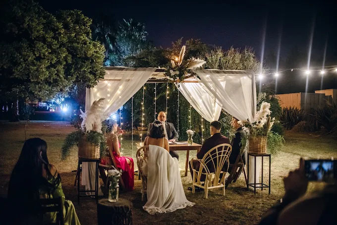 Ceremonia de casamiento de noche en el parque, bajo una pérgola con cortinas blancas y luces