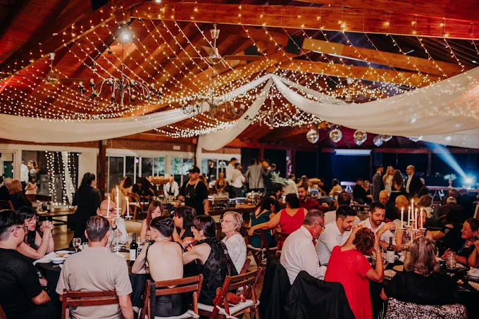 El salón de noche, con invitados cenando bajo telas blancas y guirnaldas de luces