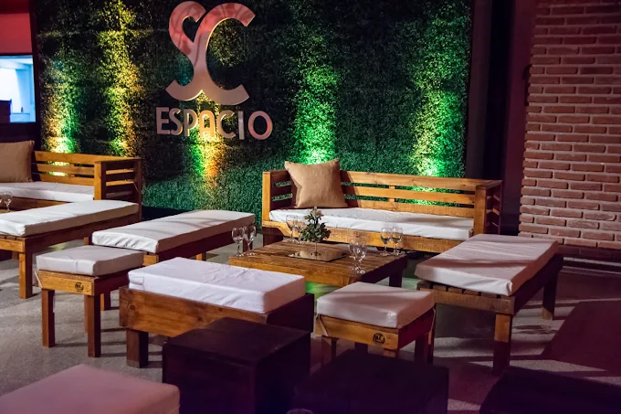Living de sillones de pallet con almohadones blancos frente a una pared verde con el logo de Espacio San Carlos