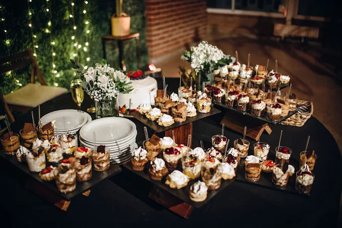 Mesa dulce con copas de postre, torta y flores blancas iluminada con luces cálidas